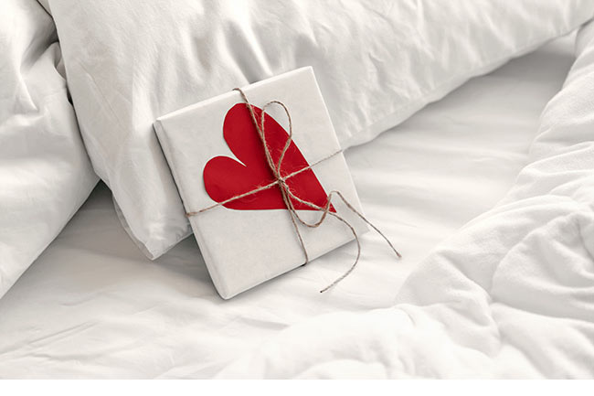 Geschenk mit Herz in weißer Leinenbettwäsche